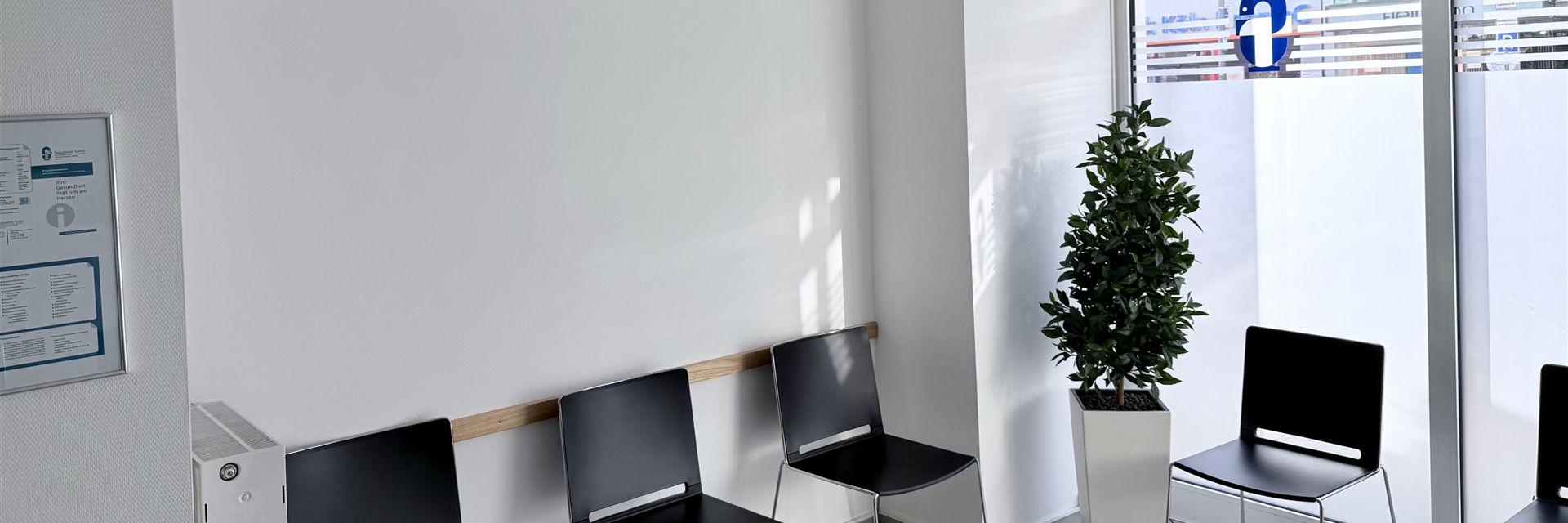 Modernes, minimalistisches Wartezimmer mit einer Reihe schwarzer Stühle und einem dekorativen Topfpflanze.